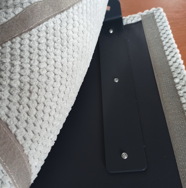 May include: A textured light gray fabric panel with a beige border, partially folded back to reveal a smooth black interior panel. The black panel features a vertical strip with three evenly spaced silver-toned metal rivets or fasteners.
