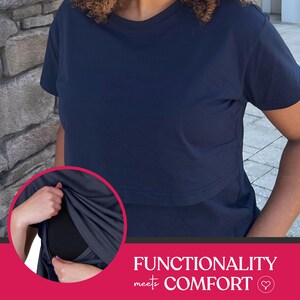 May include: A solid navy blue short-sleeved t-shirt featuring a horizontal flap across the chest. An inset circular image shows the flap lifted to reveal a black fabric layer underneath. The text "FUNCTIONALITY meets COMFORT" is printed below.