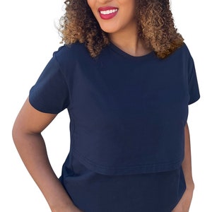 May include: A solid navy blue short-sleeved t-shirt featuring a horizontal overlay panel across the chest, paired with blue denim shorts that have a frayed, raw-edge hemline. The t-shirt has a classic crew neckline and a simple, clean design.