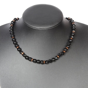 May include: A black beaded necklace with copper accents. The necklace is on a black display stand.