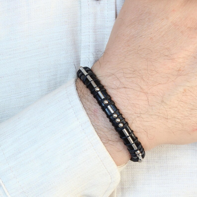 May include: A black leather bracelet with silver accents and small metal beads.