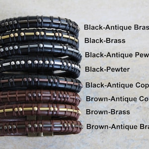 May include: A stack of eight leather bracelets with different metal accents. The bracelets are black and brown leather with gold, silver, and copper accents. The bracelets are arranged in a stack from top to bottom, with the black bracelets on top and the brown bracelets on the bottom. The bracelets are labelled with their colour and metal accents.