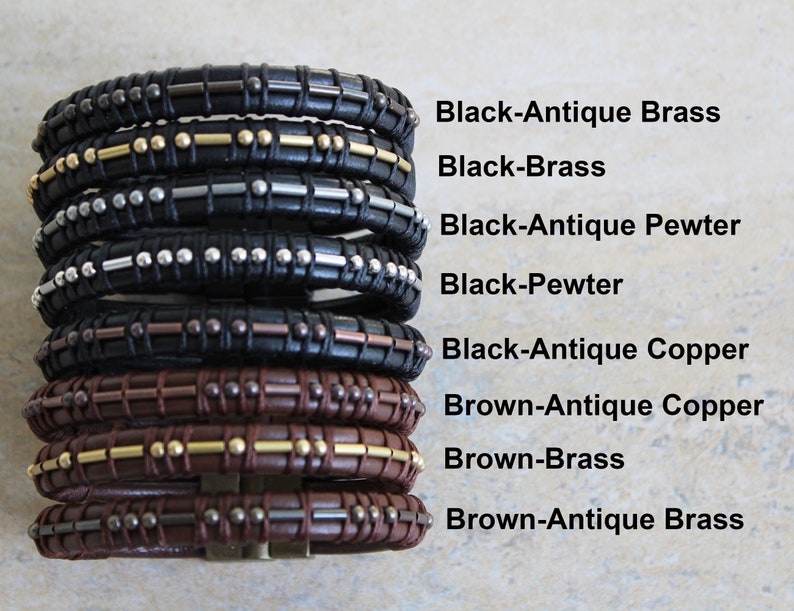 May include: A stack of eight leather bracelets with different metal accents. The bracelets are black and brown leather with gold, silver, and copper accents. The bracelets are arranged in a stack from top to bottom, with the black bracelets on top and the brown bracelets on the bottom. The bracelets are labelled with their colour and metal accents.