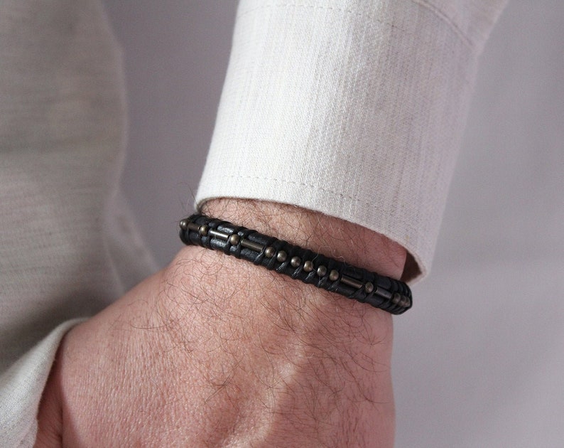 May include: A black leather bracelet with silver accents. The bracelet is woven and has a subtle texture.