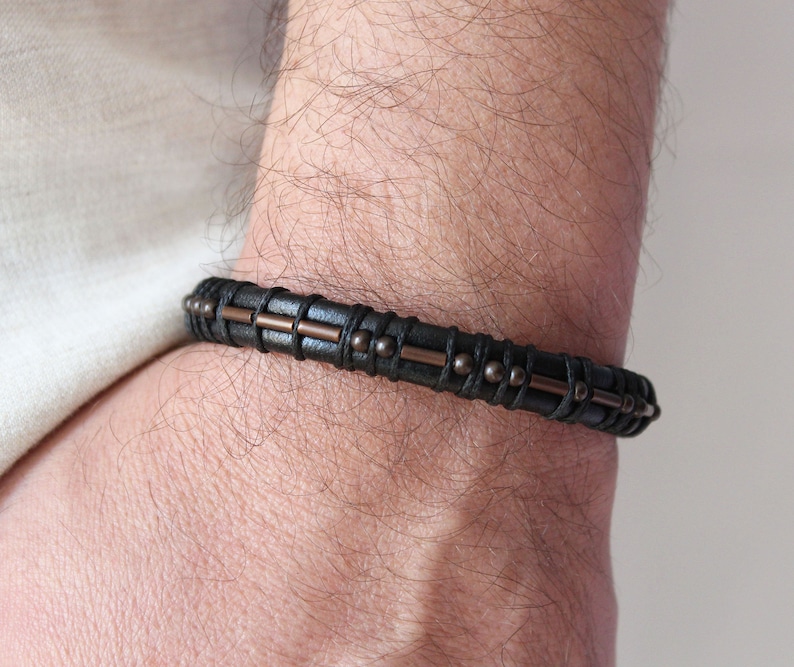 May include: A black leather bracelet with copper accents and small beads.