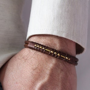 May include: A brown leather bracelet with gold beads and a metal bar accent.