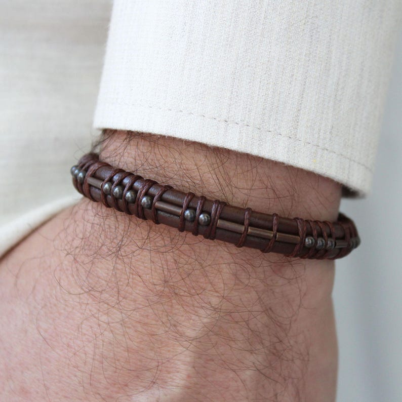 May include: A brown leather bracelet with metal accents. The bracelet has a woven design and is adorned with small metal beads.