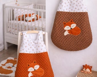 May include: A sleeveless baby sleeping bag featuring a white top section with a small brown floral pattern and a textured brown minky bottom section. An embroidered sleeping fox applique is centred on the front of the brown fabric.