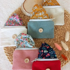 Op de afbeelding: Een verzameling van vijf kleine ritszakjes gemaakt van geribbelde corduroy stof in wit, vergrijsd blauw, roze en rood. Elk tasje heeft een voering met bloemenpatroon en een ronde houten knoop met de tekst Handmade with Love.