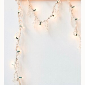May include: A white string of lights with a frayed texture, wrapped around a wooden dowel rod. The lights are strung on a white cord and have a warm white glow.