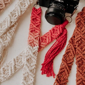 May include: Three camera straps made of macrame with different color combinations. The straps are made of cotton cord and have a tassel at the end. The straps are shown with a black camera with a MINOLTA lens.