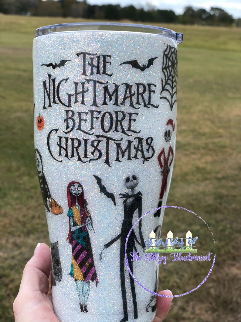 May include: White glitter tumbler with a black and white image of characters from the movie "The Nightmare Before Christmas". The text "The Nightmare Before Christmas" is printed on the tumbler.
