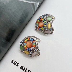 May include: A pair of silver earrings with colorful beads and stones. The earrings are shaped like a crescent moon and have a variety of colors, including green, blue, orange, and pink.