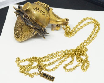 May include: A gold heart-shaped pendant with a crown of thorns and the word "Mafia" inscribed on it. The pendant is attached to a gold chain with a small tag that reads "MAFIA".