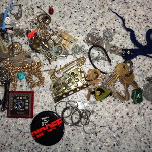 May include: A collection of assorted trinkets and keys, including a gold chain, a blue lighter, a red and white pin with the text "Right to Work is a Ripoff", a small silver key chain with a blue and white charm, and a silver key chain with a silver charm that says "The University of Connecticut".
