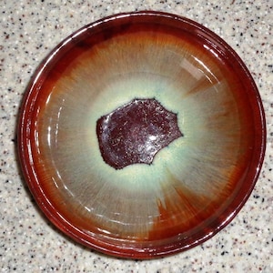 Könnte beinhalten: Eine Keramikschüssel mit brauner, weißer und grüner Glasur. Die Schüssel hat ein einzigartiges, abstraktes Design mit einer dunkelbraunen Mitte.