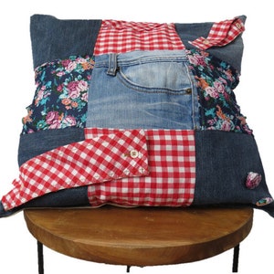 Op de afbeelding: Een patchwork kussenhoes gemaakt van hergebruikt denim en rood-wit geruit stof. De kussenhoes heeft een bloemenprint en een denim zak.