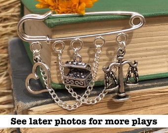 May include: Silver charm bracelet with a heart, a treasure chest, and a scale of justice. The bracelet is attached to a safety pin, making it a unique and stylish accessory.