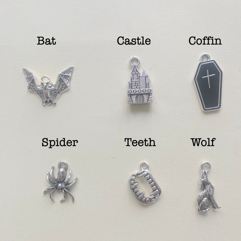 May include: Six silver charms with Halloween themes. The charms are bat, castle, coffin, spider, teeth, and wolf.