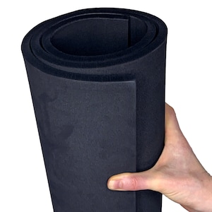 May include: A rolled up black foam sheet, approximately 1/2 inch thick, being held by a hand. The foam is textured and appears to be a type of soundproofing material.