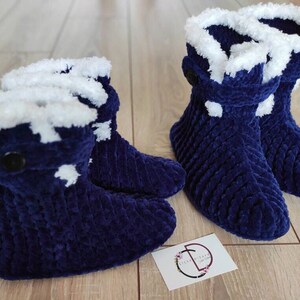 Può includere: Coppia di pantofole blu e pelose con bordo bianco e un dettaglio a bottone. Le pantofole sono realizzate in un materiale morbido e soffice e hanno una vestibilità comoda.