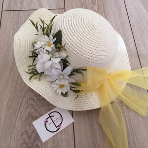 May include: A white straw hat with a yellow ribbon and white flowers. The hat is on a wooden surface.
