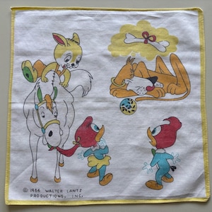 Op de afbeelding: Een wit katoenen zakdoek met een gele rand heeft een cartoonillustratie van een paard, een konijn, een hond en twee vogels. De tekst "© 1964 WALTER LANTZ PRODUCTIONS, INC." is gedrukt in de linkerbenedenhoek.