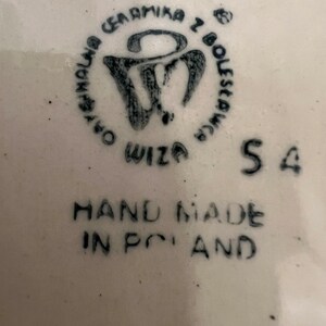 May include: A white ceramic plate with a black stamp that reads "Ceramika z Boleslawca" and "Wiza" with a stylized "W" logo. The plate also has the text "HAND MADE IN POLAND" and the number "54" printed on it.