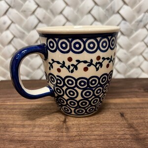 May include: A white ceramic mug with a blue and brown floral pattern. The mug has a rounded shape and a handle.