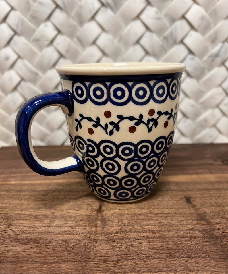 May include: A white ceramic mug with a blue and brown floral pattern. The mug has a rounded shape and a handle.