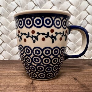 May include: A white ceramic mug with a blue and brown floral design. The mug has a blue handle and a wide, rounded base.