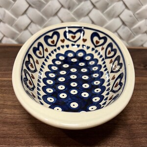 May include: A white oval ceramic bowl with a blue and brown pattern. The bowl has a repeating pattern of blue circles with white centers and a border of brown hearts.