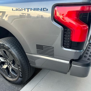 May include: A gray pickup truck with the word "LIGHTNING" in blue lettering. A black and white American flag sticker is on the side. The taillight is red. The tire is black with the word "YEAR" on the sidewall.