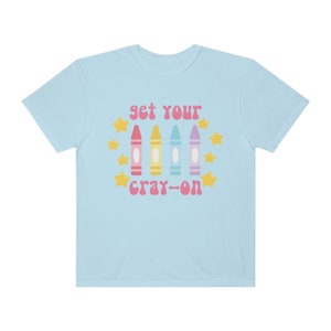 May include: Light blue t-shirt with the text "get your cray-on" in pink and yellow letters. The text is surrounded by yellow stars and four colourful crayons.