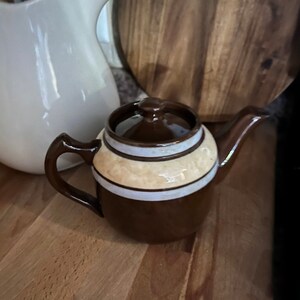 May include: A brown and white striped teapot with a lid. The teapot has a rounded body and a spout on the side.