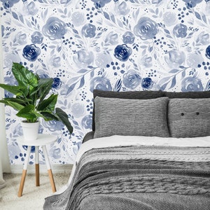 May include: A bedroom with a bed with a gray knitted blanket and two gray pillows. The wall behind the bed is covered in blue floral wallpaper.