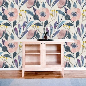 Op de afbeelding: Een witte kast met glazen deuren en twee planken staat voor een muur die bedekt is met een bloemig behangpatroon. Het behang heeft roze bloemen met blauwe centra en groene bladeren op een cr&egrave;mekleurige achtergrond.