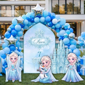 Op de afbeelding: Een feestachtergrond met een grote boog met de naam Aurora en het cijfer 7, omringd door een blauwe ballonslinger met zilveren sterballonnen. Drie uitgesneden figuren van een blond personage in een blauwe jurk en een sneeuwpop.