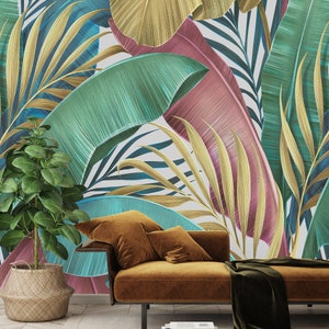 May include: A brown velvet sofa with two pillows sits in front of a wall with a tropical leaf pattern. The leaves are in shades of green, blue, pink, and gold.