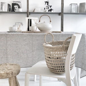 May include: A neutral-toned interior scene featuring a white teapot with a wooden handle, a woven basket, and a striped tablecloth. The shelves above display books and decorative items, creating a minimalist aesthetic.