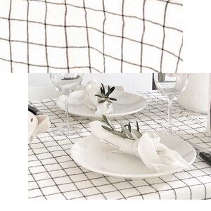 May include: White linen tablecloth with a black grid pattern. The table is set with white plates, napkins, and glassware. The text "Linen checks!" is written in cursive at the bottom of the image.