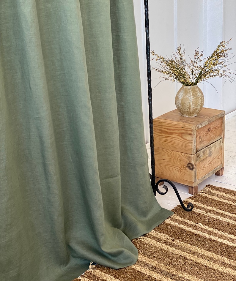 Pode incluir: Uma cortina de linho verde-s&aacute;lvia pendurada na frente de uma mesa auxiliar de madeira com um vaso de flores secas. A cortina est&aacute; reunida na parte inferior e a mesa &eacute; feita de madeira recuperada.