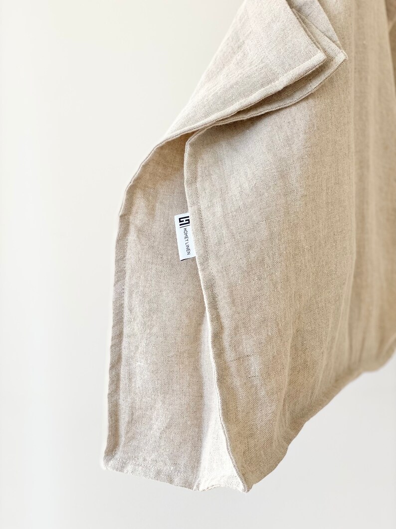 Może przedstawiać: Beżowa lniana tkanina, złożona, z etykietą "HONEY LINEN". Tkanina ma teksturowany wygląd, prawdopodobnie do tekstyli&oacute;w domowych, takich jak ręczniki lub serwetki. Neutralny kolor i naturalny materiał sugerują skupienie się na prostocie i zr&oacute;wnoważonym rozwoju.