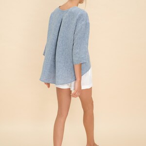 May include: A light blue linen top with three-quarter sleeves and a pleated back detail. The top is paired with white shorts and brown sandals. The outfit is casual and suitable for warm weather.