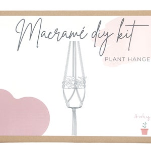 May include: A brown cardboard box with a white label that says "Macrame DIY Kit Plant Hanger" with a pink watercolor background and a line drawing of a macrame plant hanger. The box also has a small illustration of a potted plant with the word "onkyuu" written above it.