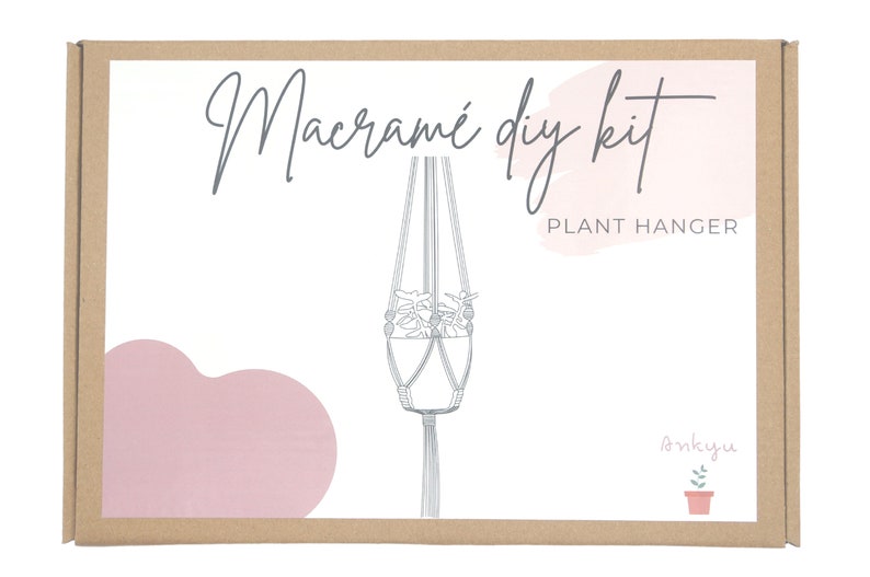 May include: A brown cardboard box with a white label that says "Macrame DIY Kit Plant Hanger" with a pink watercolor background and a line drawing of a macrame plant hanger. The box also has a small illustration of a potted plant with the word "onkyuu" written above it.