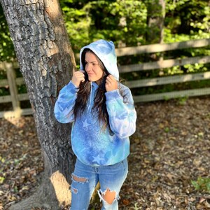 May include: A blue and white tie-dye hoodie with stars. The hoodie has a drawstring hood and a relaxed fit.