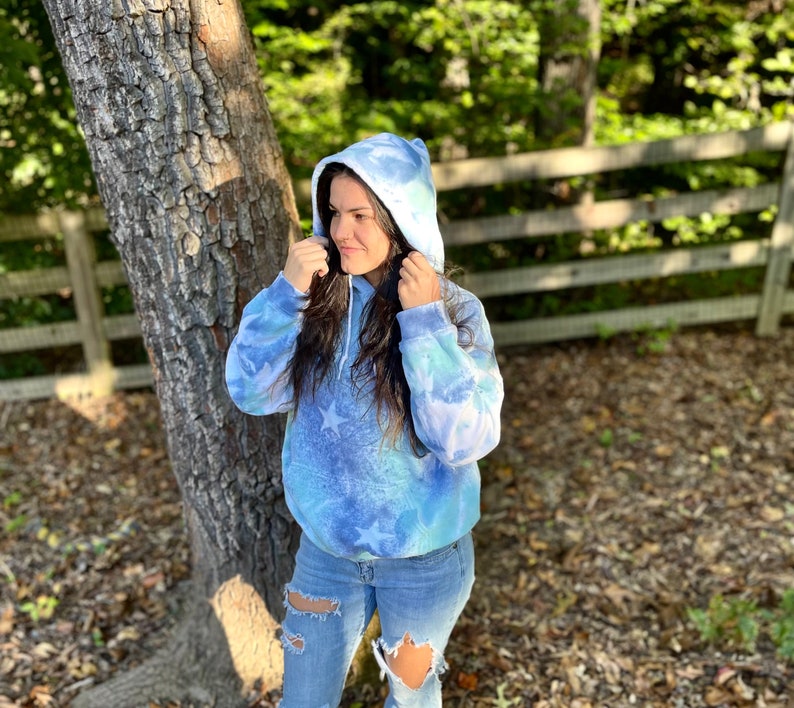 May include: A blue and white tie-dye hoodie with stars. The hoodie has a drawstring hood and a relaxed fit.