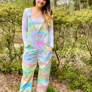 Könnte beinhalten: Eine Frau trägt einen Batik-Overall mit einem weißen Langarm-Shirt darunter. Der Overall hat ein hellblaues, gelbes, rosa und weißes Batik-Muster.