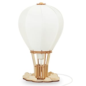 Può includere: Lampada decorativa a mongolfiera con paralume bianco e struttura in legno. La lampada poggia su una base a forma di nuvola e ha un cavo di alimentazione bianco. La lampada è alta circa 30 cm.